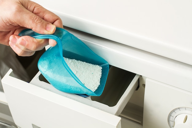 A man pours soap powder into the tray of the washing machine