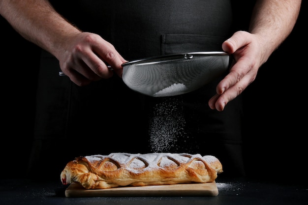 Man powders sugar on pie on dark background