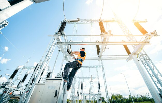 A man on a power line wearing a safety harness and a yellow shirt is climbing a power line.