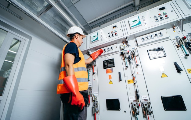 Photo a man in a power plant wearing a safety vest and red gloves stands in front of a panel with the words'power'on it.