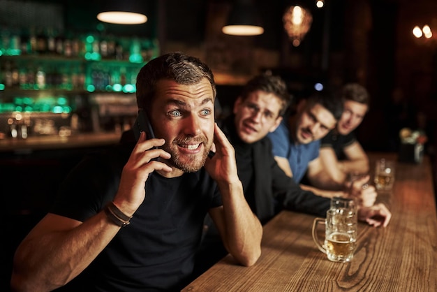 Man praat aan de telefoon Drie sportfans in een bar kijken naar voetbal met bier in de hand
