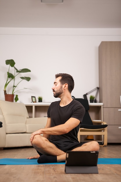 Man praat met zijn meisje tijdens een videogesprek terwijl hij yogahoudingen aan het uitwerken is in de woonkamer