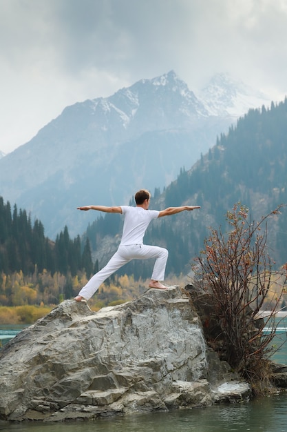 男は山を背景にヨガを練習します。 Virabhadrasana2または戦士をポーズします。