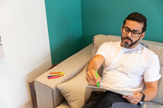 Man practicing art therapy sitting in the living room of his
home painting and drawing with colore