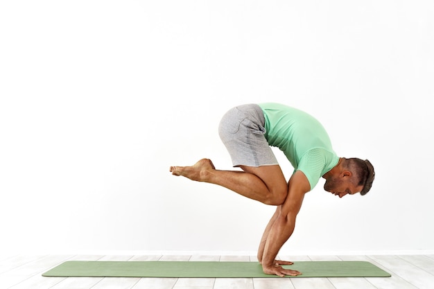 Man practicing balance yoga pose on white studio 