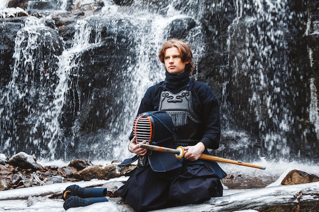 Man practicing kendo with bamboo sword on waterfall background