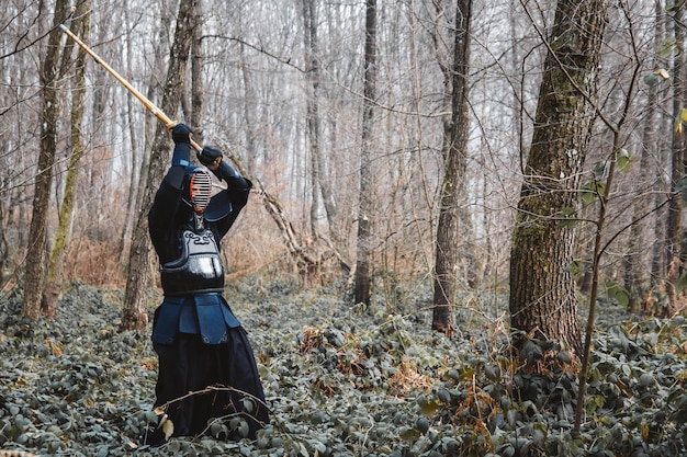 Man practicing kendo with shinai bamboo sword on forest background