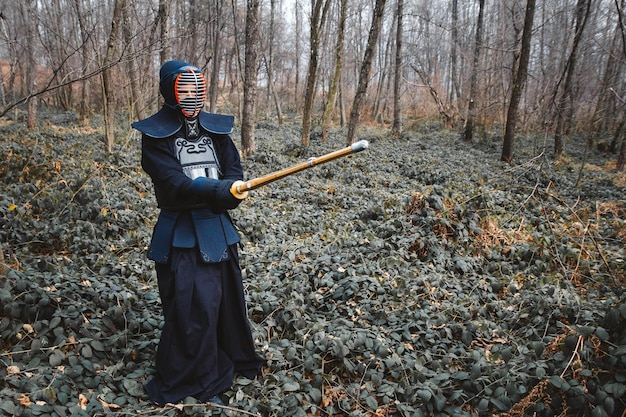 Man practicing kendo with shinai bamboo sword on forest background