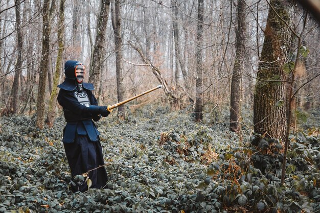 写真 森の背景に竹刀で剣道を練習する男