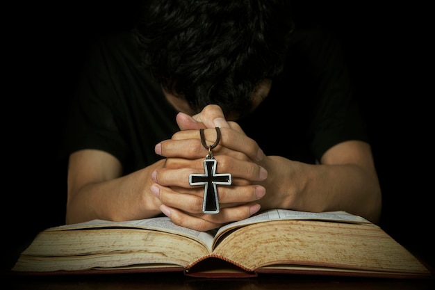 Мужчина молится с библией и крестом