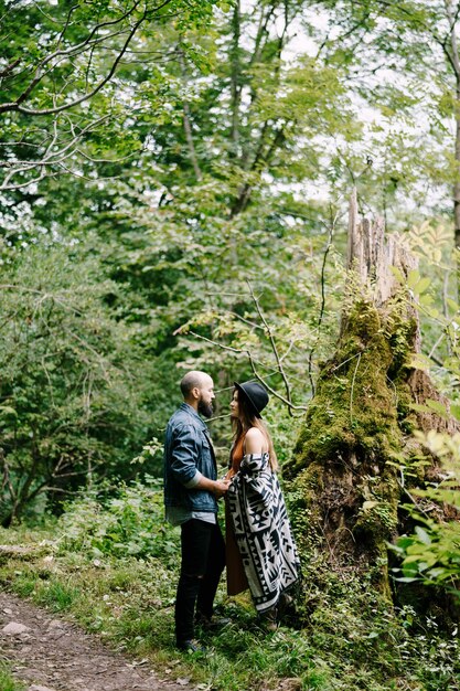 Man and pregnant woman stand near mossy tree near path in park