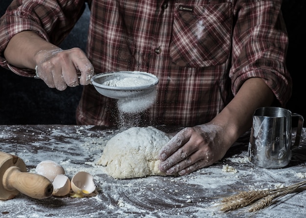 Man preparing bread dough on wooden table in a bakery close up