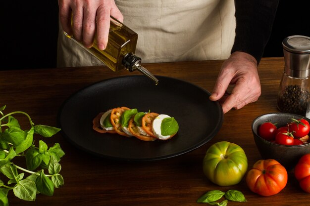 Foto uomo che prepara un'insalata caprese su un piatto nero