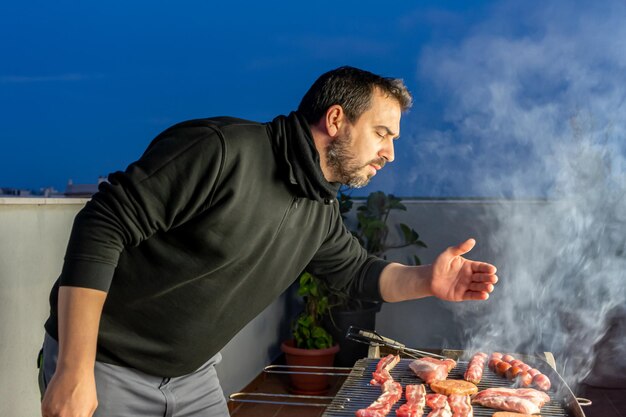 Foto uomo che prepara il cibo sulla griglia al barbecue contro il cielo sulla terrazza