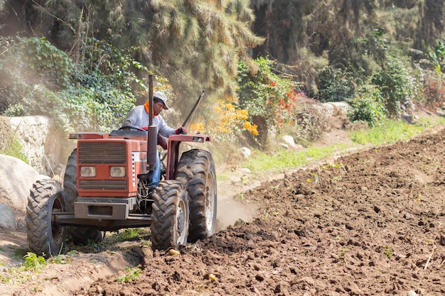 Мужчина готовит землю к уборке с помощью трактора на ферме