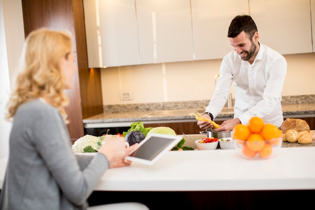 Man preparing a meal while a young woman sitting and use of tablets in a modern kitchen