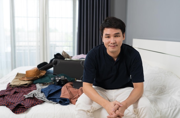 Man preparing and packing clothes into suitcase on bed at home holiday travel concept