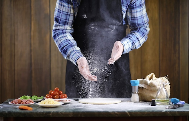 Un uomo che prepara una pizza, impasta l'impasto e mette gli ingredienti