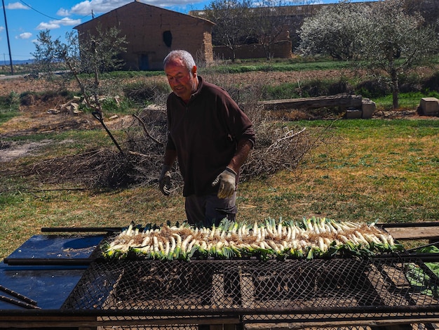 Man preparing a row of calsots typical Catalan sweet onions to grill on the barbecue