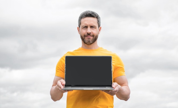 Man presenting pc on sky background copy space