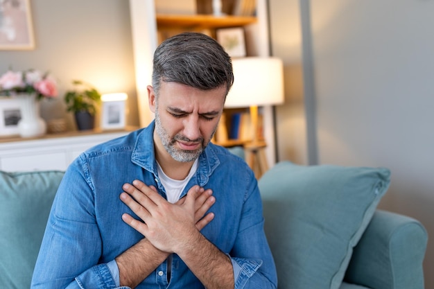 Photo man presses hand to chest has heart attack suffers from unbearable pain mature man with pain on heart in living room man suffering from bad pain in his chest heart attack at home