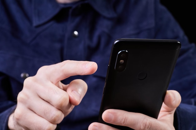 Man presses his finger on the screen of a smartphone on a dark background