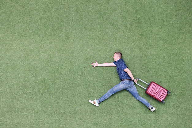 Man pretend to run on green summer grass with suitcase