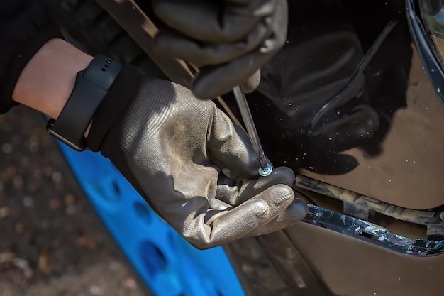 man probeert autobumper te repareren Schroeven in schroevendraaier voor bevestiging hand in zwarte handschoen