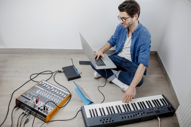 Man produce electronic soundtrack or track in project at home. Male music arranger composing song on midi piano and audio equipment in digital recording studio.