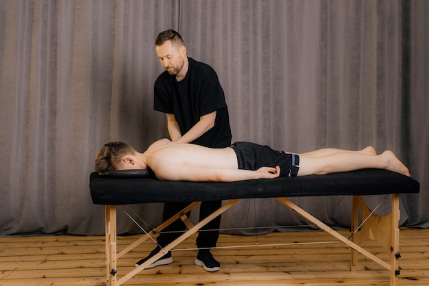 Man professional doctor osteopath fixing and stretching mans back with hands during exersicing at