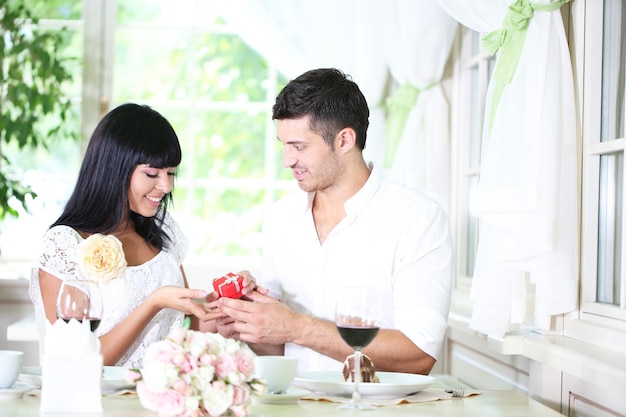 Мужчина предлагает и держит обручальное кольцо своей женщине над столом в ресторане