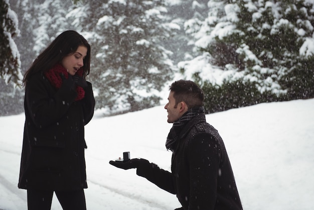 Man proposing to woman with ring in forest during winter