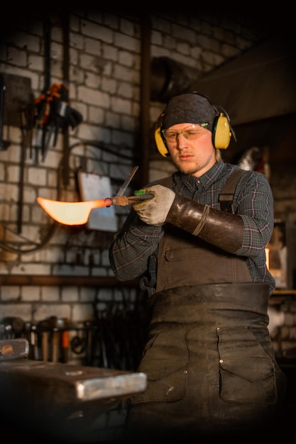 A man in protecting headphones holding hot metal knife sample in the forceps