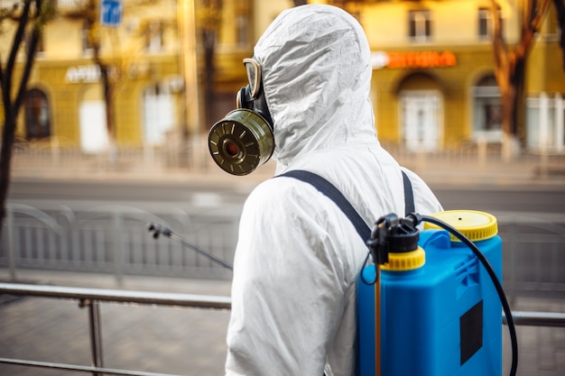 Uomo in equipaggiamento protettivo che disinfetta la città