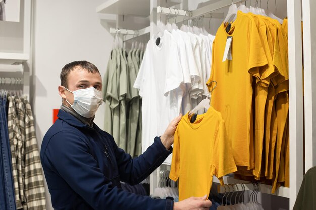 A man in a protective face mask chooses casual clothes Clothing store Retail trade