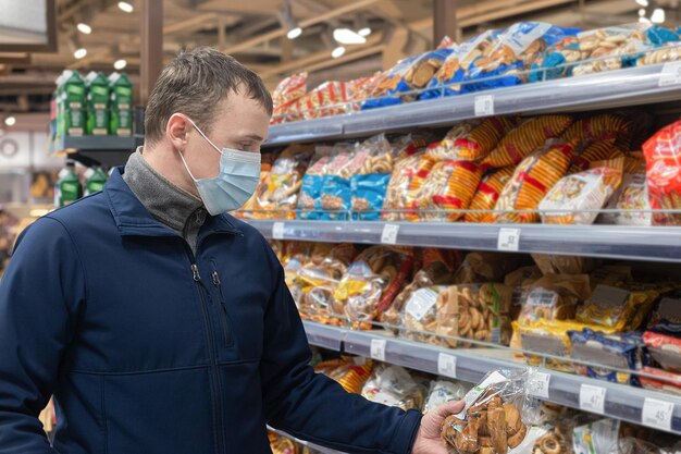 A man in a protective face mask chooses products in the store Food and drinks Quarantine