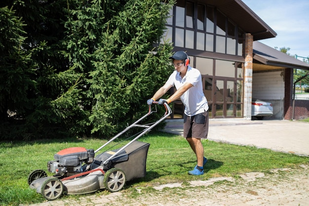 Man in protective headphones and glasses mowing the grass