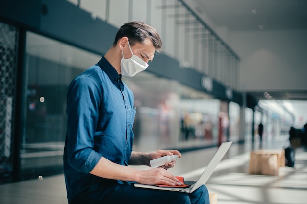 Man in a protective mask disinfects his laptop