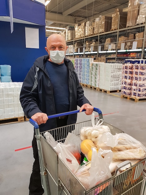 A man in a protective mask take a shopping cart with products in a supermarket during a pandemic of a coronavirus