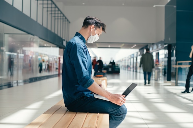 Man in a protective mask works on a laptop near a city building.