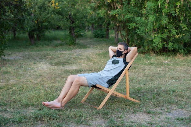 man in protective medical mask on his face sunbathing lawn person relaxing on lounge sunbed in garden