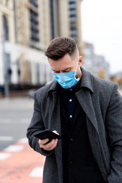 Man in protective medical mask using mobile phone walking in the city. Responsible behavior during world covid-19 pandemic.