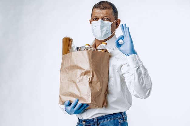 食料品店からの袋で防護マスクの男。食品配達