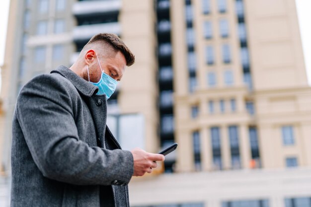 Man in protective medical wear using mobile phone walking in\
the city responsible behavior during world covid19 pandemic