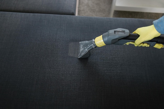 Человек в защитной резиновой перчатке чистит диван профессиональным методом извлечения с моющим пылесосом