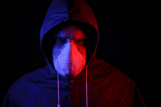 Un uomo con una tuta protettiva in gomma e una maschera medica bianca. protezione dal virus. illuminato in rosso e blu.