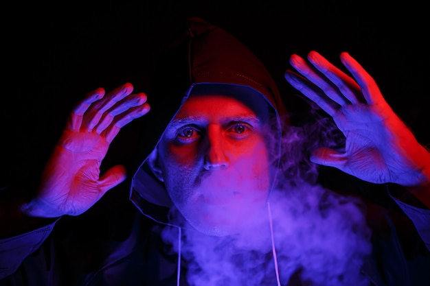 A man in a protective suit exhales smoke. Halloween image concept. Virus protection. Illuminated with colored lights