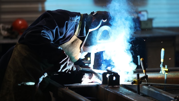 A man in a protective suit and mask welds pieces of iron