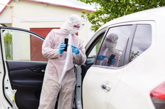 L'uomo in tuta protettiva, maschera medica e guanti di gomma per la protezione da batteri e virus sta guidando un'auto. maschera protettiva durante la quarantena, pandemia mondiale, covid 19, coronavirus, infezione.