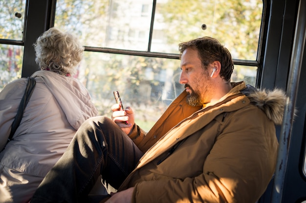 Man in public transport sitting with smartphone listening to music